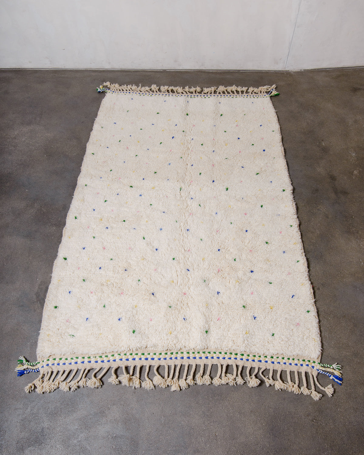 Berberlin Beniourain rug in cream wool with coloured dots laying on concrete floor.